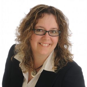 woman with curly hair and black glasses smiling at the camera