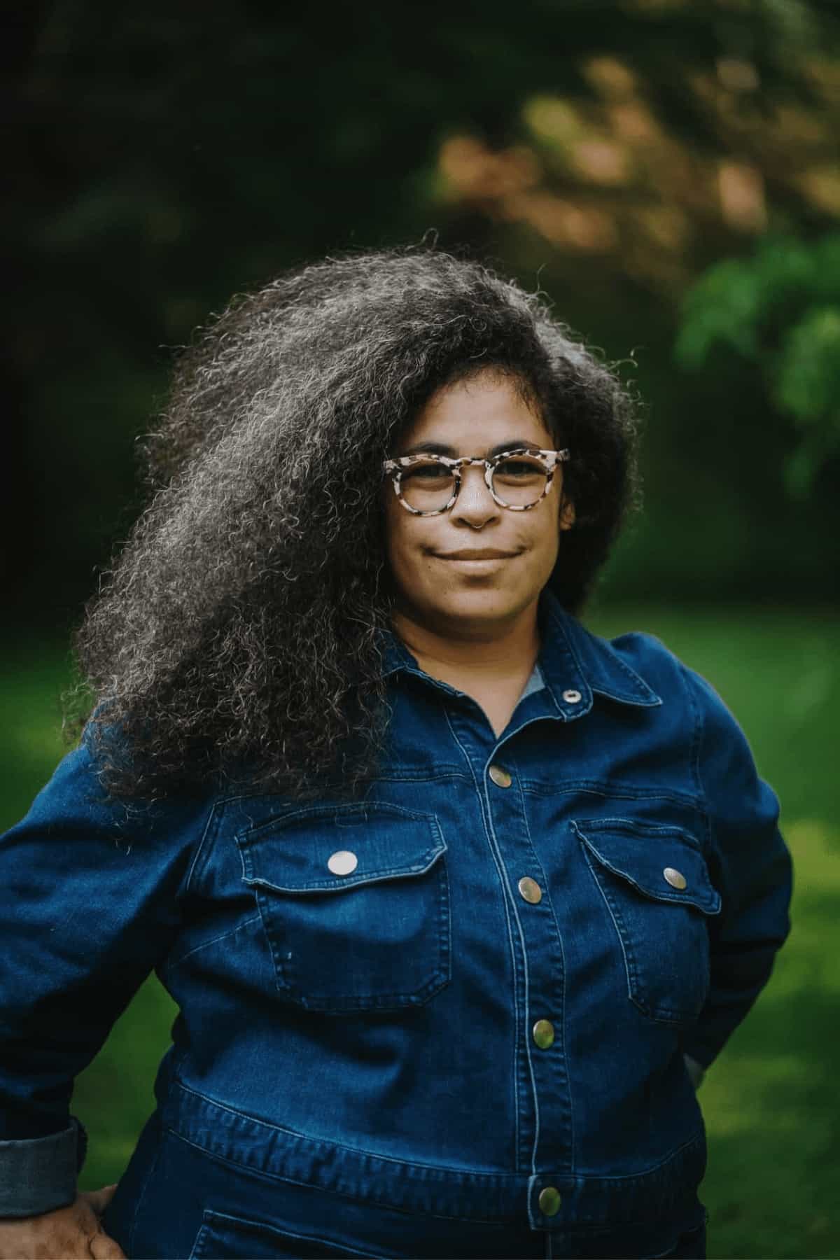 woman in blue button up with glasses smiling to the camera