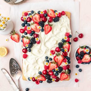 sheet cake on a pink surface topped with lots of berries and chamomile flowers