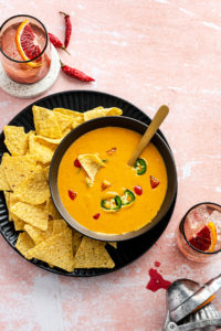 bowl of queso with chips on a plate on a pink surface