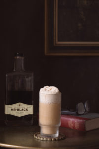 a glass with a cocktail sitting on a desk with a book and glasses