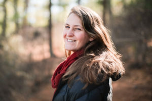 headshot of a woman half turned smiling at the camera in a red scarf