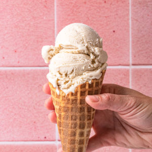 person holding an ice cream and ice cream cone in front of a pink tile wall