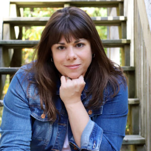 woman in jean jacket sitting on steps holding head under chin