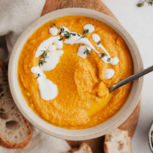 Pumpkin carrot soup in a bowl with a spoon and three slices of bread in the background