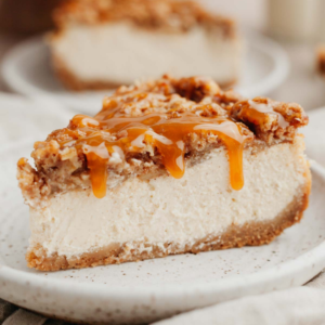 Slice of cinnamon cheesecake topped with caramel drizzle and cinnamon apples on a white plate