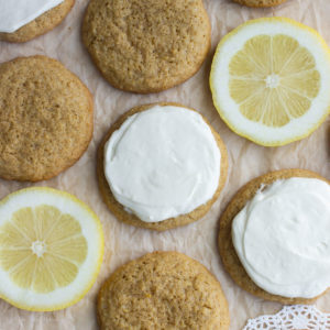 lemon cheesecake cookies on a baking sheet with frosting and two slices of lemons
