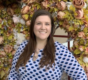 woman with brown hair smiling and flowers in the background