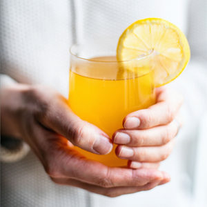 two hands holding a glass of tea with a lemon wedge