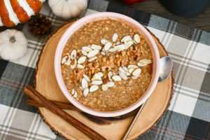 pumpkin pie overnight oats in a bowl with nut toppings and cinnamon sticks and a spoon next to it