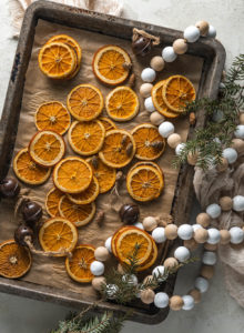 dried orange slices on a baking sheet and pan surrounded by decorations