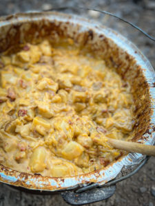 dutch oven potatoes with toppings in a aluminum bowl with a wooden spoon