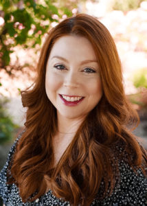 woman with ginger hair and black top smiling outdoors