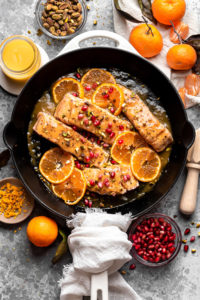 three pieces of orange glazed salmon in a pan with slices of oranges and toppings surrounded