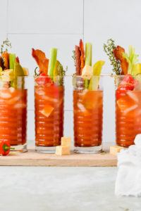 four cups of pickled bloody mary's with vegetables on a board