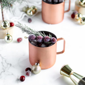 christmas themed moscow mule with sugar coated garnishes in a cup surrounded by ornament decorations