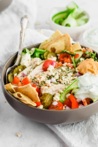 mediterranean greek salad with toppings and chips in a gray bowl and spoon