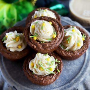 stack of espresso brownie cups with white buttercream frosting and green and yellow toppings on a gray plate