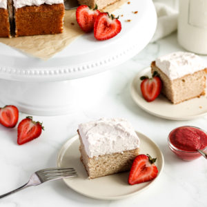 slices of strawberry cake on a plate and fork with frosting and half cut strawberries and jam