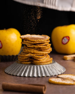 cinnamon being sprinkled over a stack of baked apple crisp