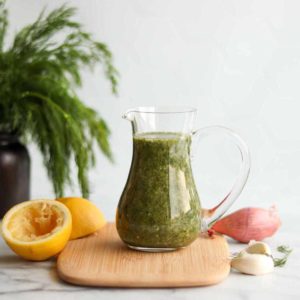 glass bottle of lemon dill salad dressing with oranges and onions surrounding it