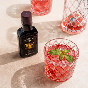 three glasses of red alcohol with topping next to a bottle of watkins