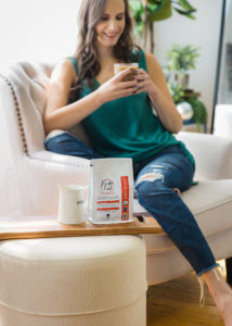 woman wearing a green shirt and jeans holding a cup of coffee and smiling