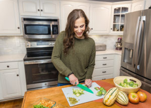 woman wearing green sweater cutting vegetables and smiling