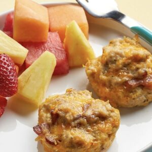 close up of two eggs balls with toppings next to cut up fruit