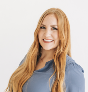 woman with long ginger hair wearing a blue blouse and smiling