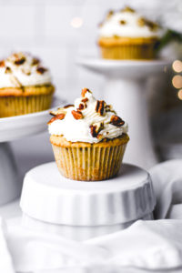 three vegan italian cream cake cupcakes with white frosting and toppings on a white stand