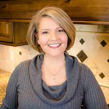 woman with short blonde hair wearing a gray sweater and smiling to the camera