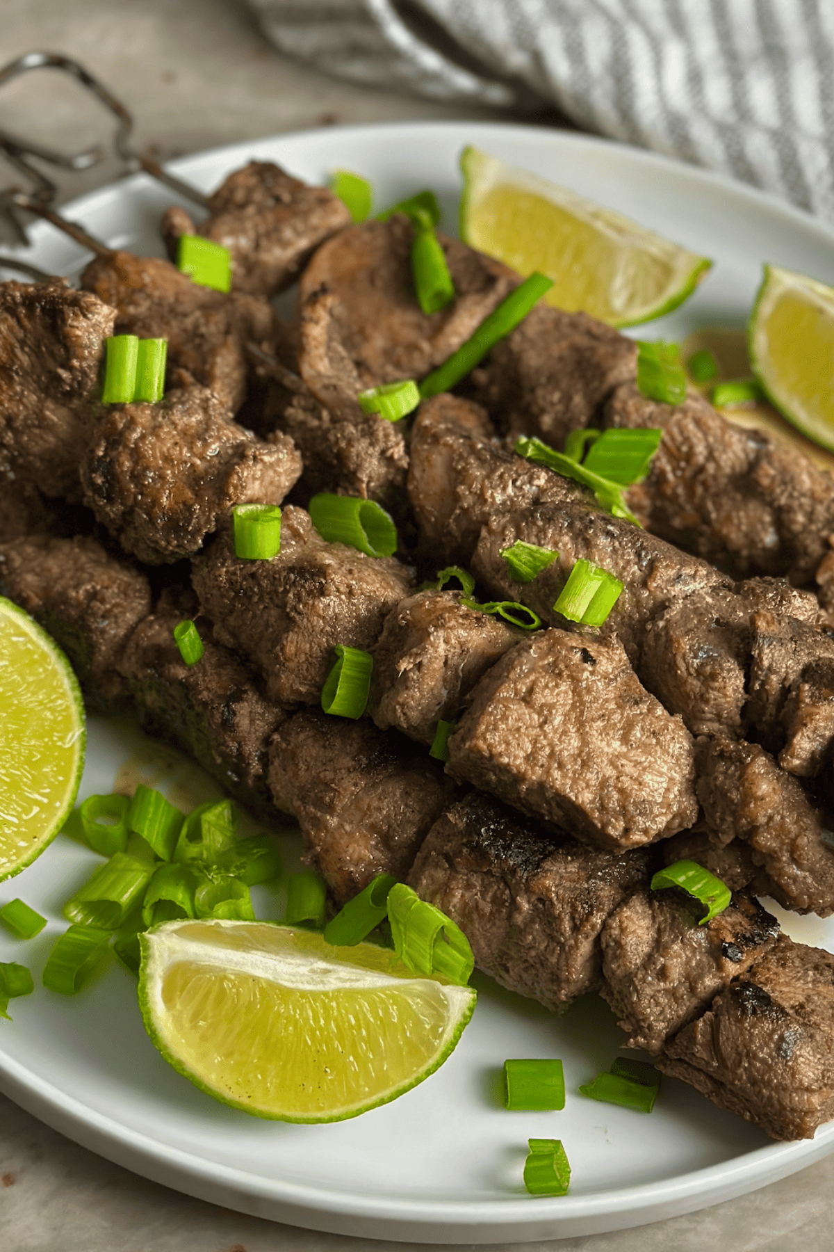 skewers of pork with lime slices on a white plate