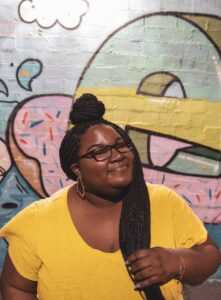 Woman in yellow shirt with long hair and glasses in front of a colorful background