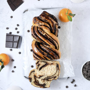 Babka with chocolate swirls slice at the end. Styled on a white background with fresh clementines and chocolate squares.