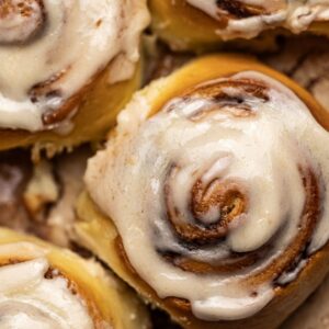 A close-up of freshly baked cinnamon rolls topped with creamy frosting, showcasing their soft, golden-brown texture and swirls of cinnamon filling.