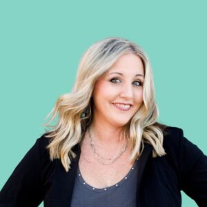 A headshot of a woman with blonde wavy hair wearing a black blazer over a gray top. She is smiling confidently in front of a solid mint green background.