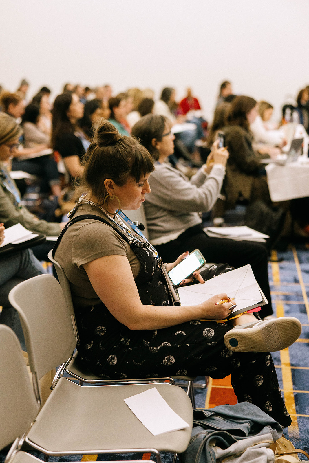 Woman taking notes during a conference session, seated among other attendees.
