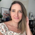 Brita Britnell smiling in a floral top, standing in a softly lit room with framed art and home decor in the background.