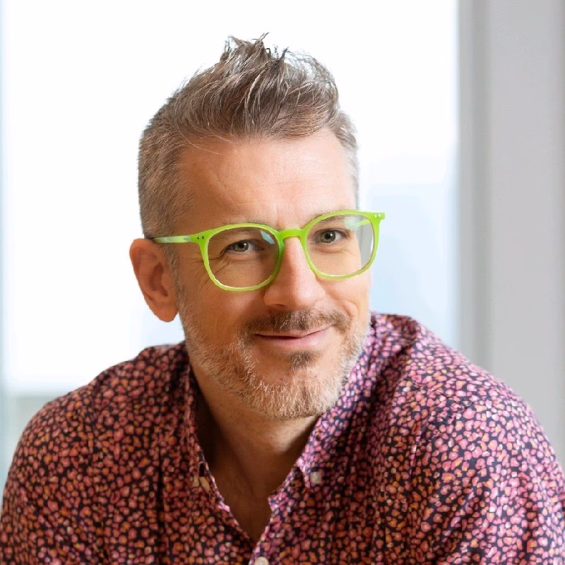 A man with short gray hair and neon green glasses smiles at the camera.